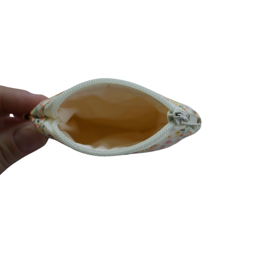 Hand holding a beige pouch with floral patterns on a white background