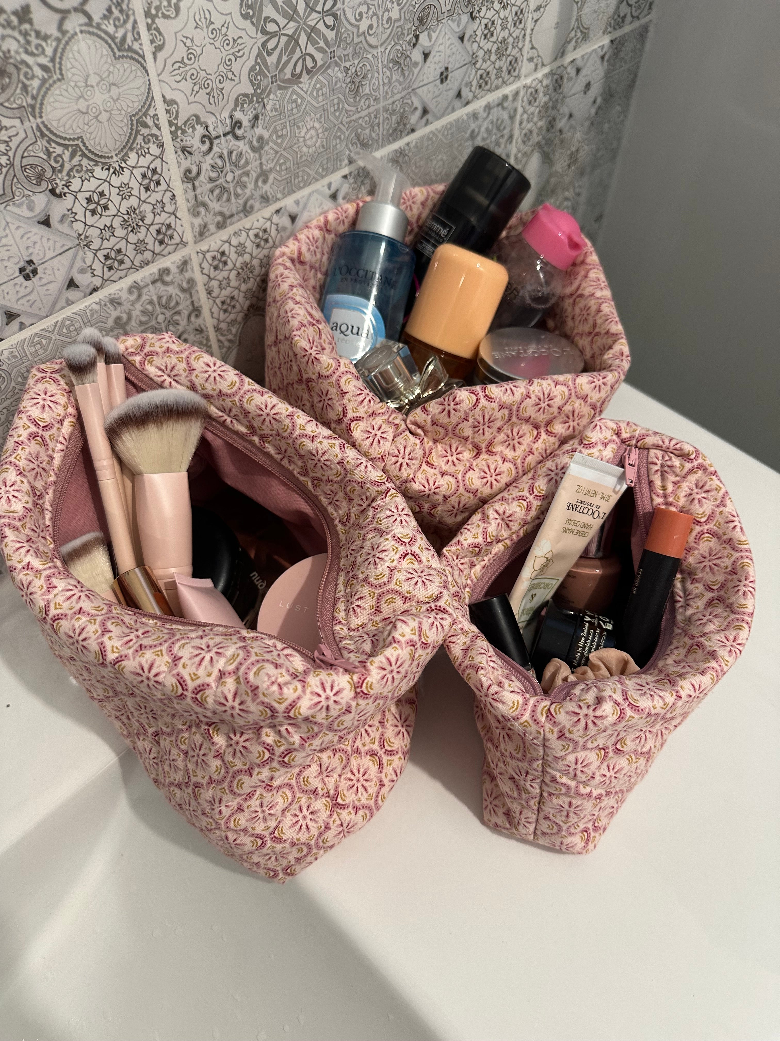 Pink floral makeup bag filled with cosmetics on a bathroom counter.