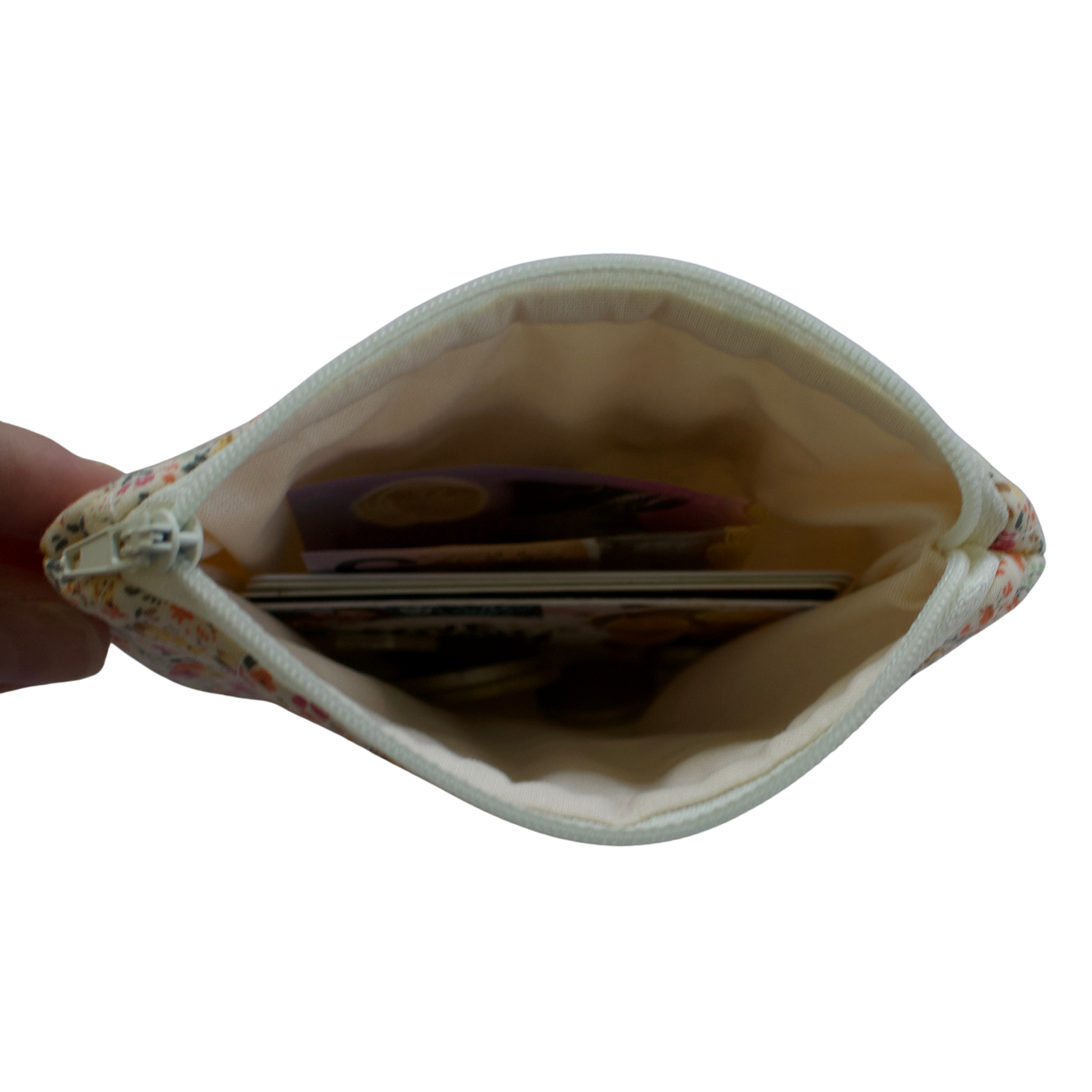 Small pouch held open by a hand, revealing coins inside on a white background