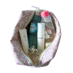 A pink and white flower makeup bag with a gold zipper, shown open and filled with various skincare and cosmetic bottles and tubes. Handmade quilted pouch. handmade cosmetic pouch. Handmade bag.