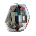 A white cosmetic bag with a red heart pattern, shown open and filled with various skincare and perfume products on a solid white background. handmade pouch. handmade cosmetic pouch. Handmade quilted pouch. Handmade bag