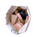 A light pink and white floral makeup bag, shown open from a top-down view, filled with various cosmetic products including brushes, a black compact, and pink tubes, on a solid white background. Handmade makeup bag. Handmade makeup pouch. quilted pouch. Quilted bag