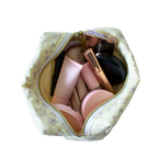 A yellow floral makeup bag filled with various cosmetic products, shown from a top-down view against a solid white background. Handmade quilted Makeup bag. Handmade makeup bag. makeup bag