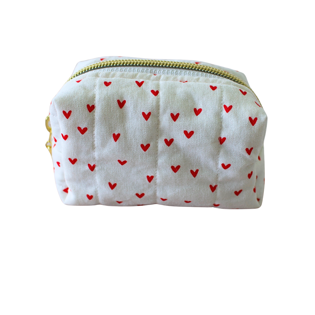 A small quilted fabric pouch with a white background and a pattern of small red hearts, featuring a gold zipper.