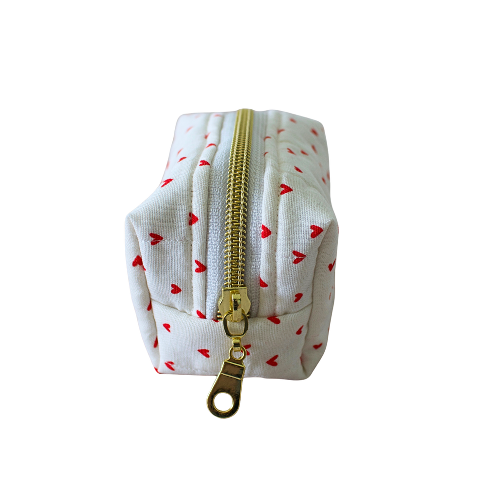 A small white fabric pouch with a repeating pattern of small red hearts and a gold zipper, shown on a plain white background.